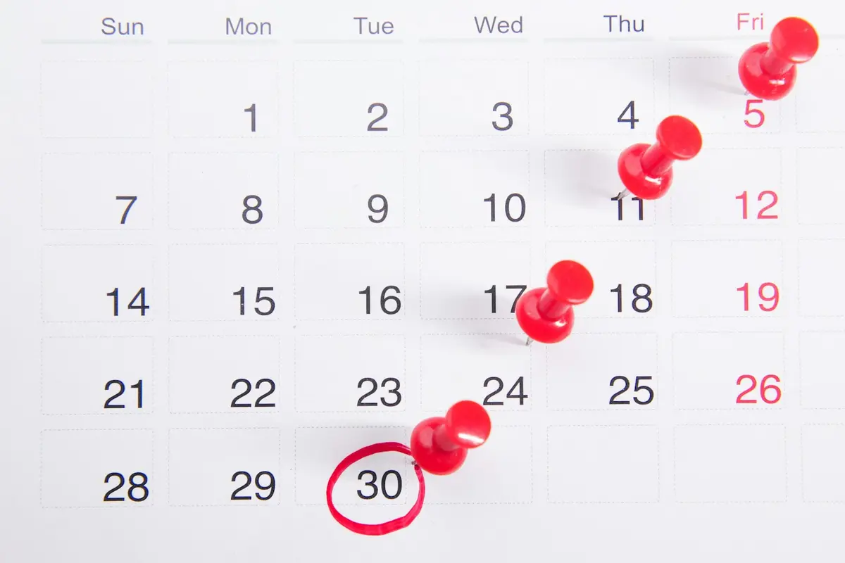 A wall calendar with four red push pins on different dates and one date circled in red