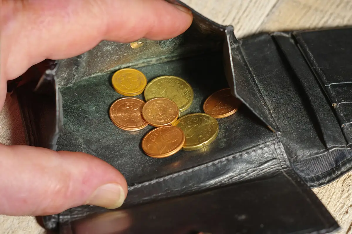 A hand holding open a worn black wallet with a few coins inside